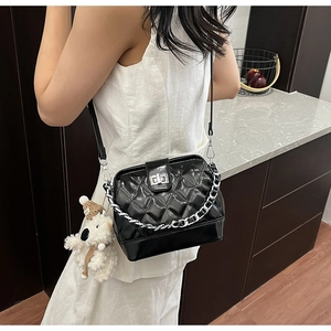 Detail view of quilted black patent leather handbag with silver chain and plush dog charm