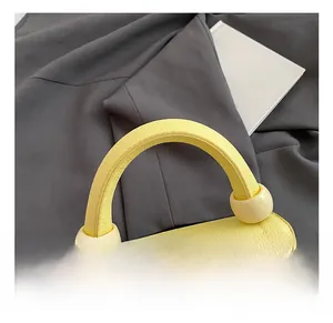 Close-up of yellow lychee grain leather bag with a unique curved handle and cream ball detail
