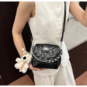 Detail of black quilted leather shoulder bag with silver chain and a cute teddy bear charm