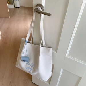 Minimalist beige canvas tote bag with blue embroidery hanging on a white door handle