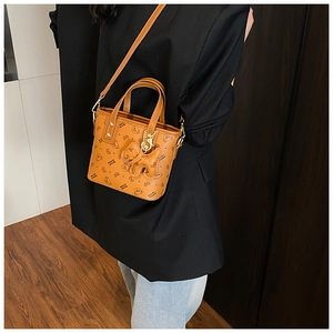 Detail of caramel brown PU leather bucket bag with bear print and bow charm on model