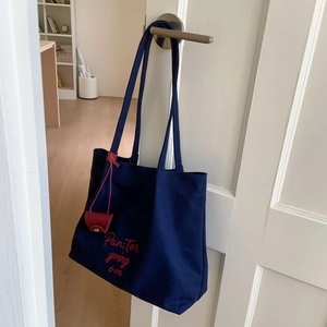 Detail of navy canvas tote bag with red Pan Tor embroidery and a red leather charm