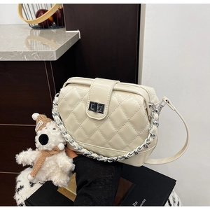 Detail of cream quilted crossbody bag with silver chain and metal clasp in lifestyle setting