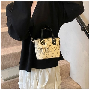 Detail shot of cream tote bag with black trim and cute bear print and dog charm