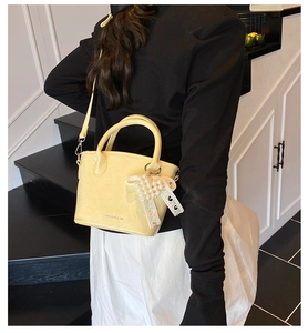 Détail d'un sac à main jaune clair en PU avec breloque cœur en perles et sangle tissée