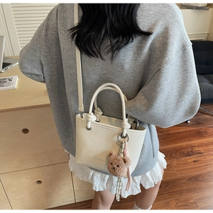 Detail of cream tote bag featuring a knotted handle and a brown plush bear charm