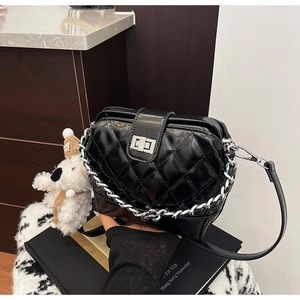 Close-up of black quilted shoulder bag with silver hardware and a white plush dog charm