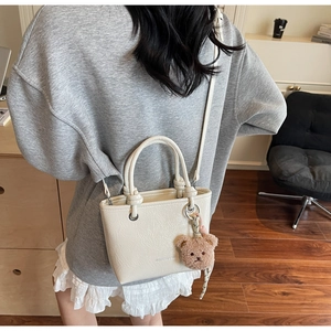 Detail of cream tote bag with lychee texture and cute brown plush bear charm