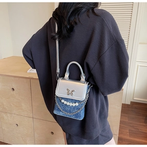 Detail of a mini denim phone bag with silver butterfly clasp and pearl chain decoration