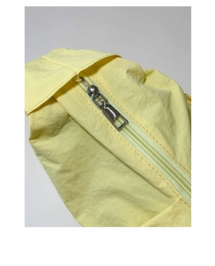 Close-up of silver metal zipper on light yellow nylon crossbody dumpling bag with folds