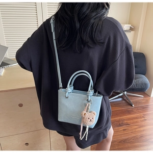Light blue faux leather tote bag with teddy bear charm shown on a model from the back