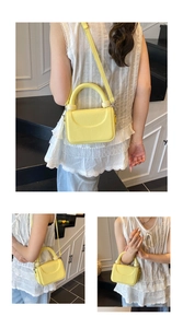 Detail view of yellow textured leather small square bag with unique round handle connectors