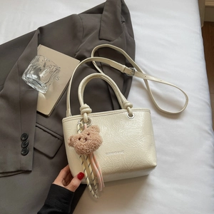 Detail of cream pleated tote bag with teddy bear charm on grey suit background