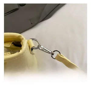 Detail eines silbernen Karabinerhakens an hellgelber Handtasche aus geprägtem Leder