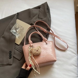 Detail of pink crinkled leather tote bag with a cute plush bear charm and adjustable strap