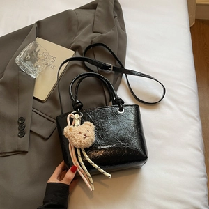 Detail of black glossy lychee texture tote bag with plush bear charm and ribbon decor