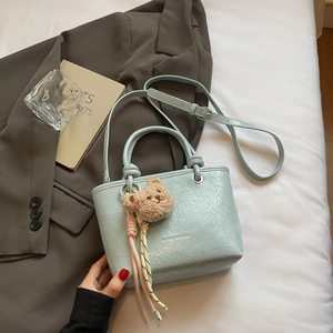 Close-up of light blue wrinkled patent leather tote bag with cute bear charm and strap