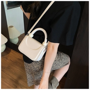 Detail view of cream-white crossbody bag with unique ball-joint handle on leather texture