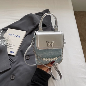 Detailed shot of silver butterfly metal buckle and pearl chain on mini crossbody bag