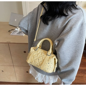 Detail of light yellow quilted handbag with silver rivets and metal shoulder strap hooks