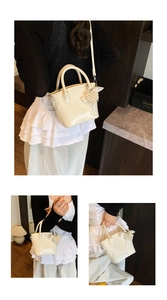 Detail der cremefarbenen Lackleder-Mini-Tote mit Herzanhänger aus Perlen und Schleife