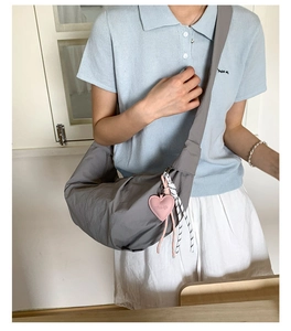 Detail der grauen Nylon-Sichel-Tasche mit breitem Gurt und pinkfarbenem Herzanhänger
