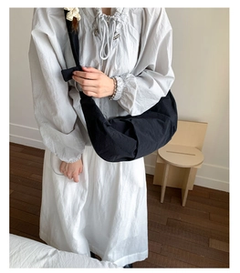 Minimalistische schwarze halbmondförmige Umhängetasche getragen zu einem grauen Baumwollkleid