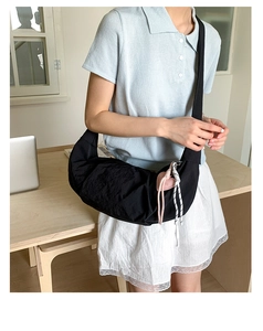 Detail of black crescent crossbody bag featuring a pink heart pendant and woven tassel detail