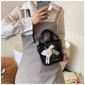 Détail du sac à main noir aspect croco avec nœud en dentelle et breloque cœur perlé