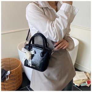 Détail d'un sac à main noir en cuir verni avec perles et ruban dans un décor cosy
