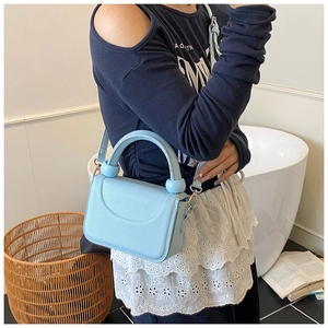 Detail of light blue crossbody bag featuring litchi texture leather and spherical handle accents