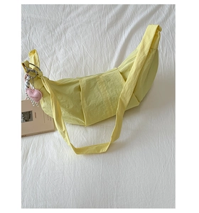 Macro detail of a bright yellow crescent nylon bag with a pink heart charm and striped strap