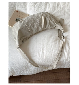 Detailed close-up of beige croissant bag with pleated fabric and metal ring on soft bedding