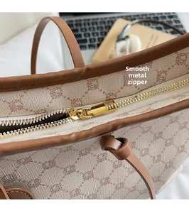 Close-up of smooth gold metal zipper on beige monogram canvas tote with leather trim