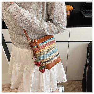 Detail of rainbow woven straw bucket bag featuring leather trim and cute strawberry charms