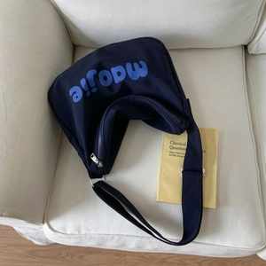 Close-up of a navy blue canvas tote bag with adjustable strap on a cream fabric sofa