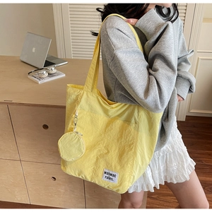 Detailed view of yellow nylon tote bag with hanging coin purse and woven text label