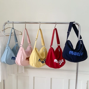 Detail of five crescent canvas crossbody bags in multiple colors on a metal rack