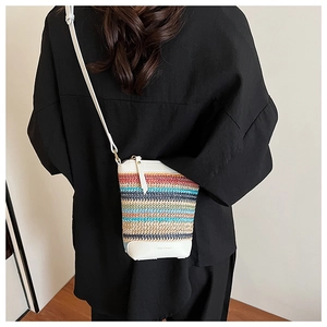 Detail of colorful woven straw bag with white leather base and shoulder strap in lifestyle setting
