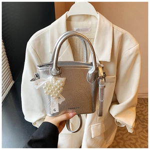 Détail du sac à main argenté plissé avec pendentif en perles et nœud en dentelle