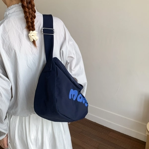 Detail of navy canvas crossbody chest bag featuring artistic blue lettering and silver buckle