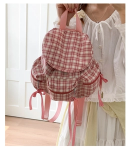 Détail du sac à dos à carreaux rouges avec des nœuds décoratifs et deux poches avant zippées