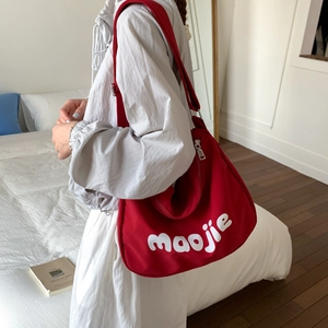Detail view of red canvas tote bag with white lettering and adjustable wide shoulder strap