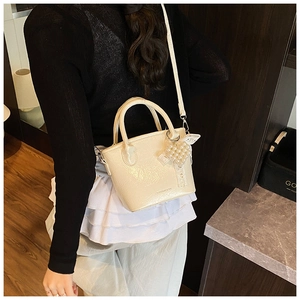 Dettaglio di una borsa a secchiello bianco crema con ciondolo a fiocco di perle e texture PU