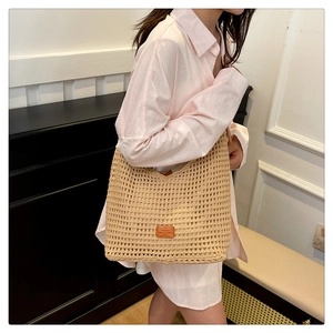 Detailed close-up of handmade woven straw tote bag with brown leather logo patch