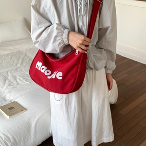 Model wearing a red canvas tote bag with white lettering and wide adjustable shoulder strap
