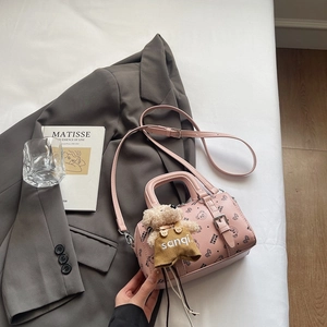 Detail der rosa Boston-Tasche mit Bärendruck und süßem Plüschbär-Anhänger auf Bett