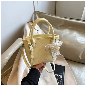 Détail d'un sac à main jaune crème avec nœud en dentelle, breloque perle et texture plissée
