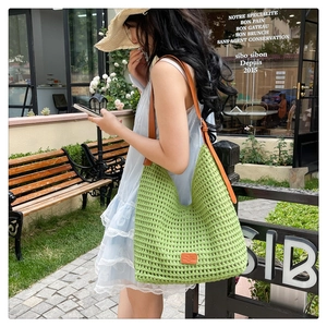 Close-up of green woven knit tote with adjustable brown leather strap and orange logo