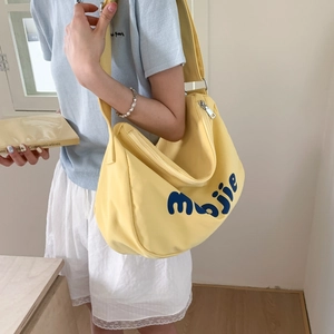 Detail of a yellow canvas tote bag featuring blue letter print and metal zipper closure